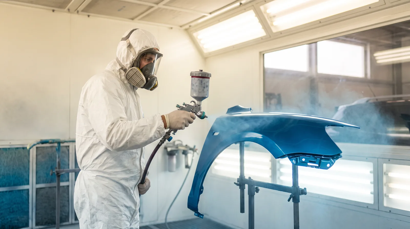 Painter spraying a car fender in a paint booth